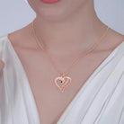 Woman wearing a rose gold heart-shaped pendant with blue and pink gemstones, engraved with the names "Sarah" and "Andrew," on a beaded chain.