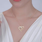 Woman wearing a gold heart-shaped pendant with blue and pink gemstones, engraved with the names "Sarah" and "Andrew," on a beaded chain.