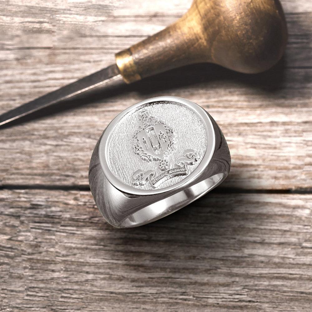 Silver signet ring with embossed family crest on wooden surface, next to an engraving tool.