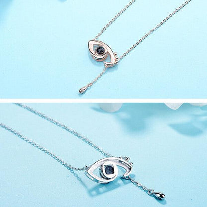 Two eye-shaped pendant necklaces, one in rose gold and the other in silver, both with dangling chains, displayed against a light blue background.